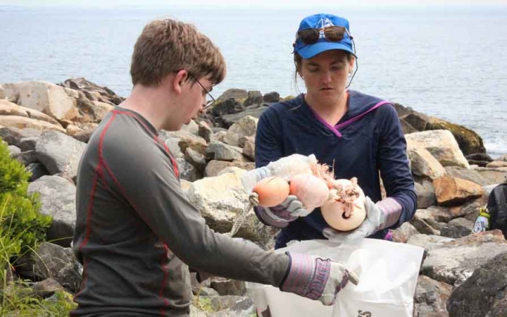 two teens pick up trash along a rocky shoreline during a service project with outward bound in maine